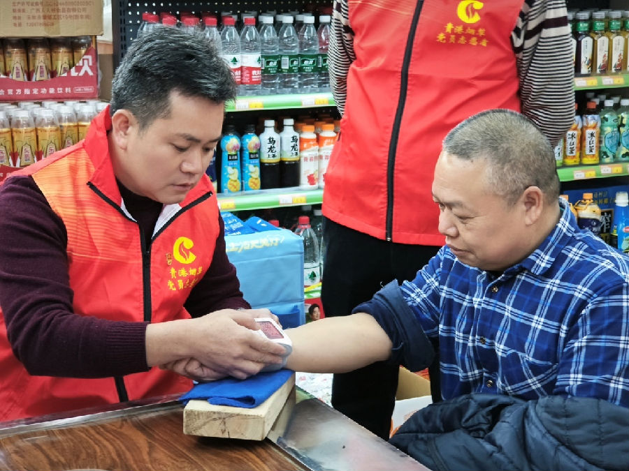 图为志愿者覃锋（右一）帮助零售户韦革明测量血压（李颖 摄）
