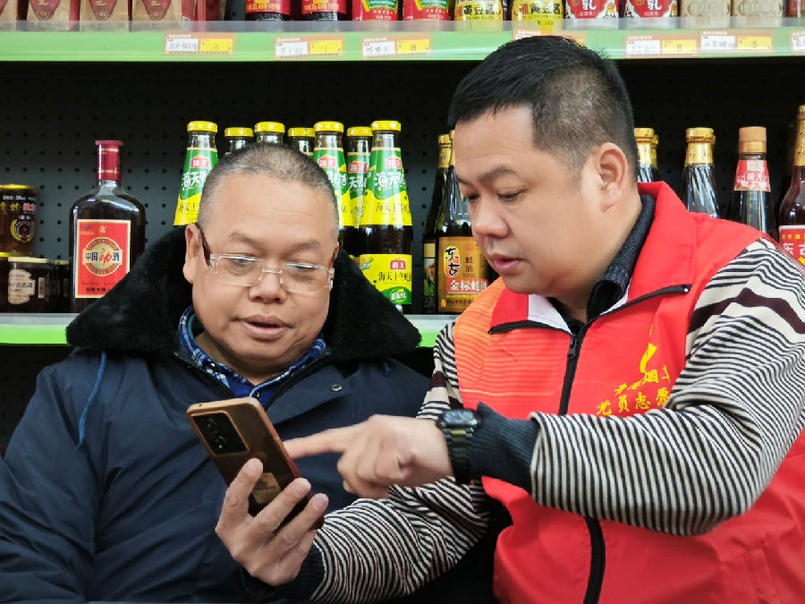 图为志愿者（左一）向零售户说明手机操作步骤（覃锋 摄）