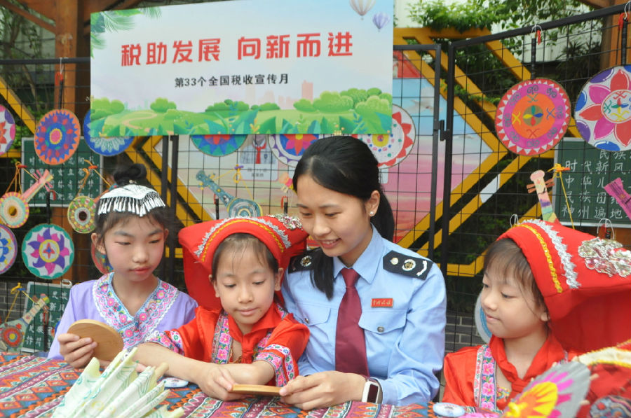 税务干部在小朋友带领下参观民族手工作品展，税务干部对小朋友进行税收知识小问答并颁发“小小税法宣传员”徽章。（石能亿 摄）
