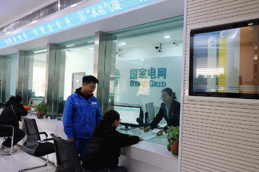 在国网阿克苏市供电公司晶水路营业厅“水电气暖”一站服务窗口，供电公司工作人员与天然气工作人员为用户办理更名过户业务。（邸敏 摄）