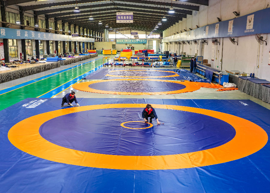 在山东泰山体育器材有限公司生产车间，工人们在检测新铺设的摔跤垫。（贾鹏 摄）