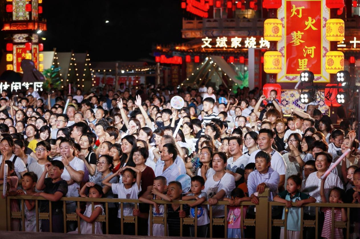 众多游客齐聚台前驻足观赏,灯火装点的古街人声鼎沸,尽显蓼河古街两周年庆典的超高人气。(王鹏 摄)